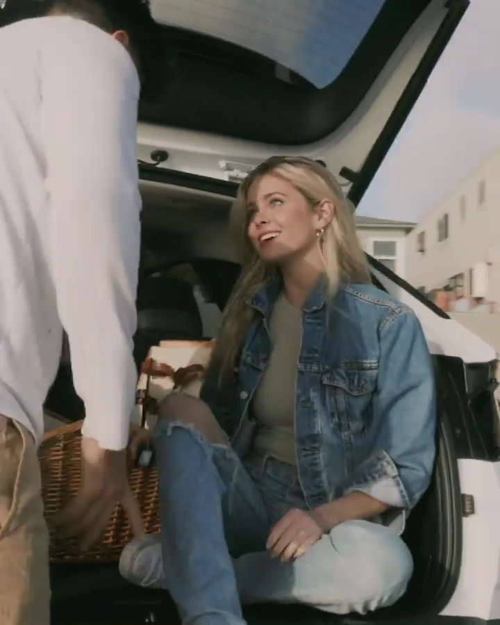 Hannah Godwin smiling while sitting in the open trunk of a white Hyundai with a picnic basket.